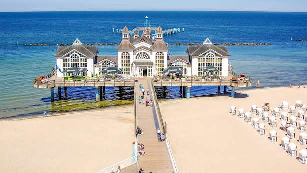 A waterfront building with a pier extending into the sea, featuring multiple levels with outdoor seating areas. - Residence Seeblick 14 with lateral Baltic Sea view - Studio beach shell / with (Sellin)
