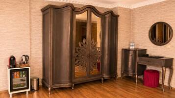 A room with a wardrobe, a desk, a mirror, and a mini-fridge.