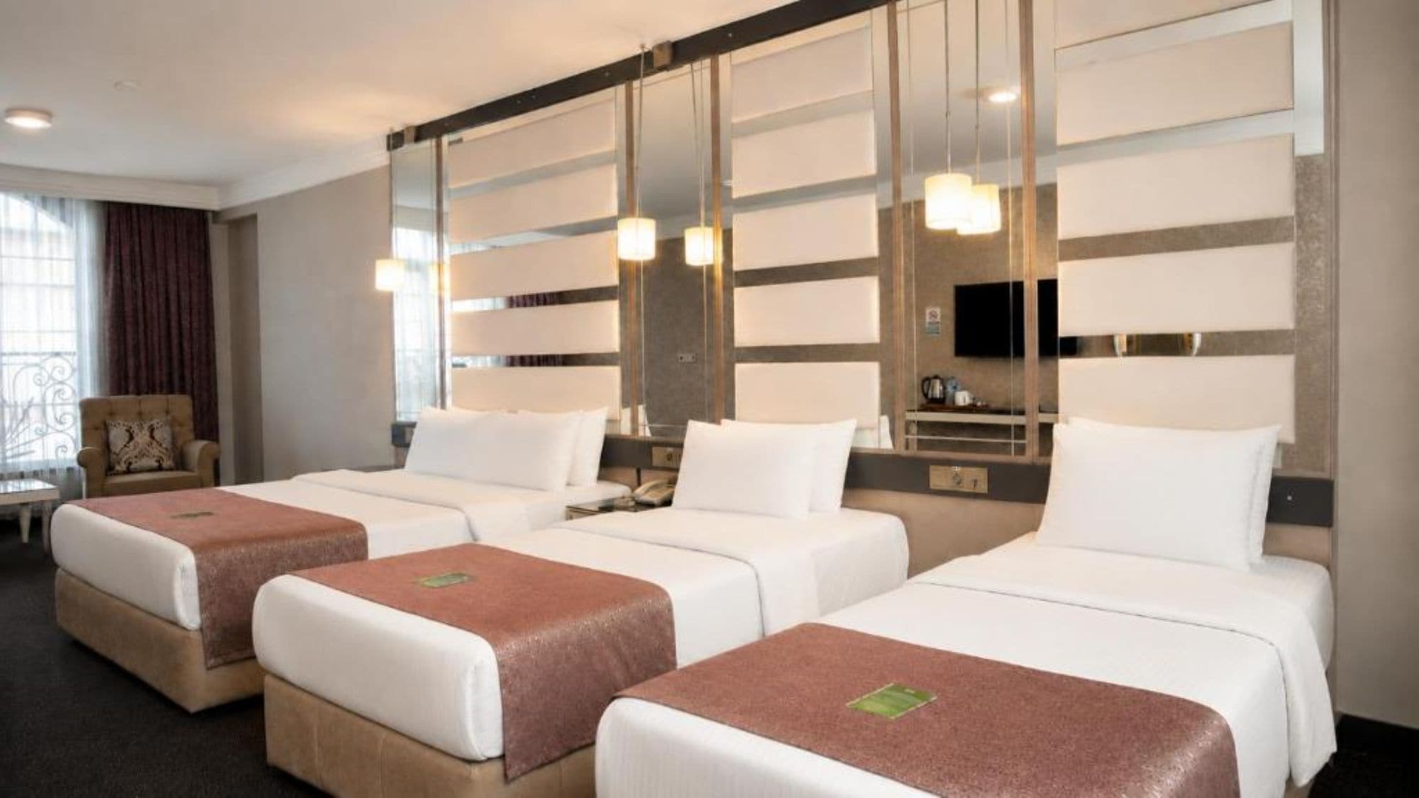 A hotel room with three beds, a sofa, a TV, and a minibar.