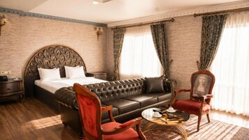 Una habitación de hotel con una cama grande, un sofá de cuero, un sillón rojo, una mesita redonda pequeña y una silla de madera clásica.