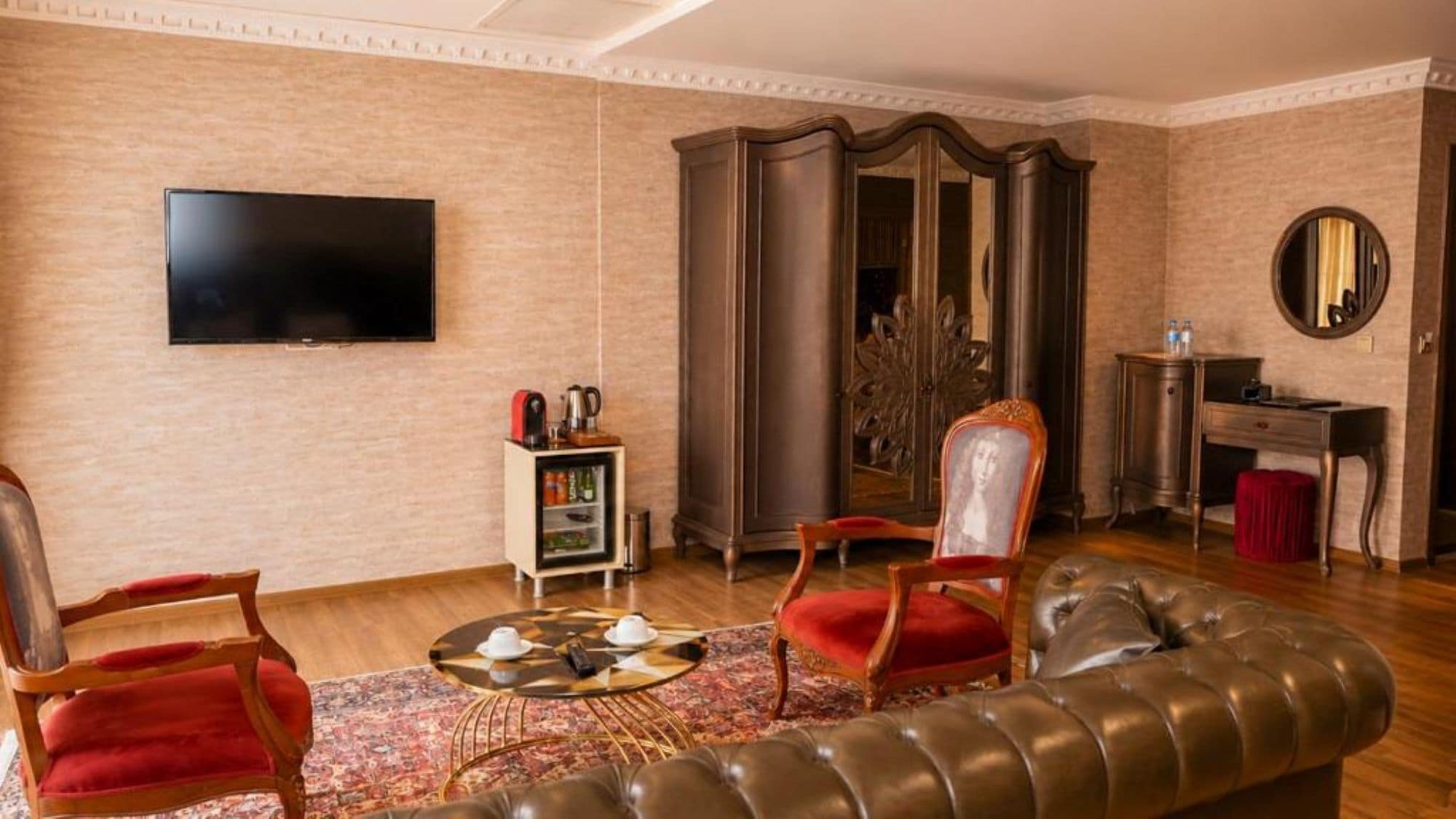 A living room with a leather sofa, two red chairs, a coffee table, a television, a cabinet, and a mirror.