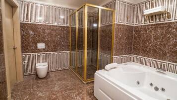 Un baño con piso de mármol, bañera, inodoro y zona de ducha con mampara de vidrio.