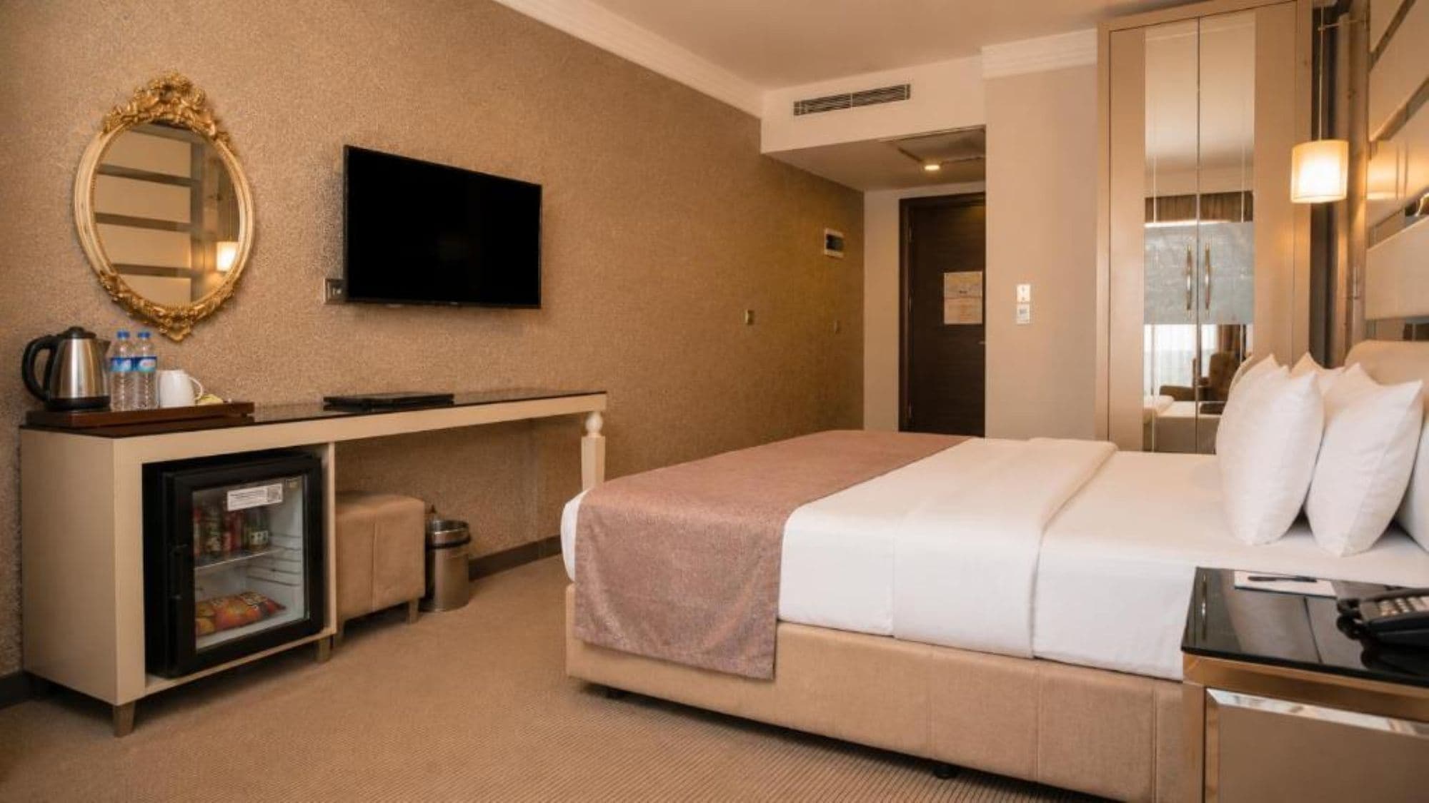 A hotel room with a bed, a television, a minibar, and a mirror.