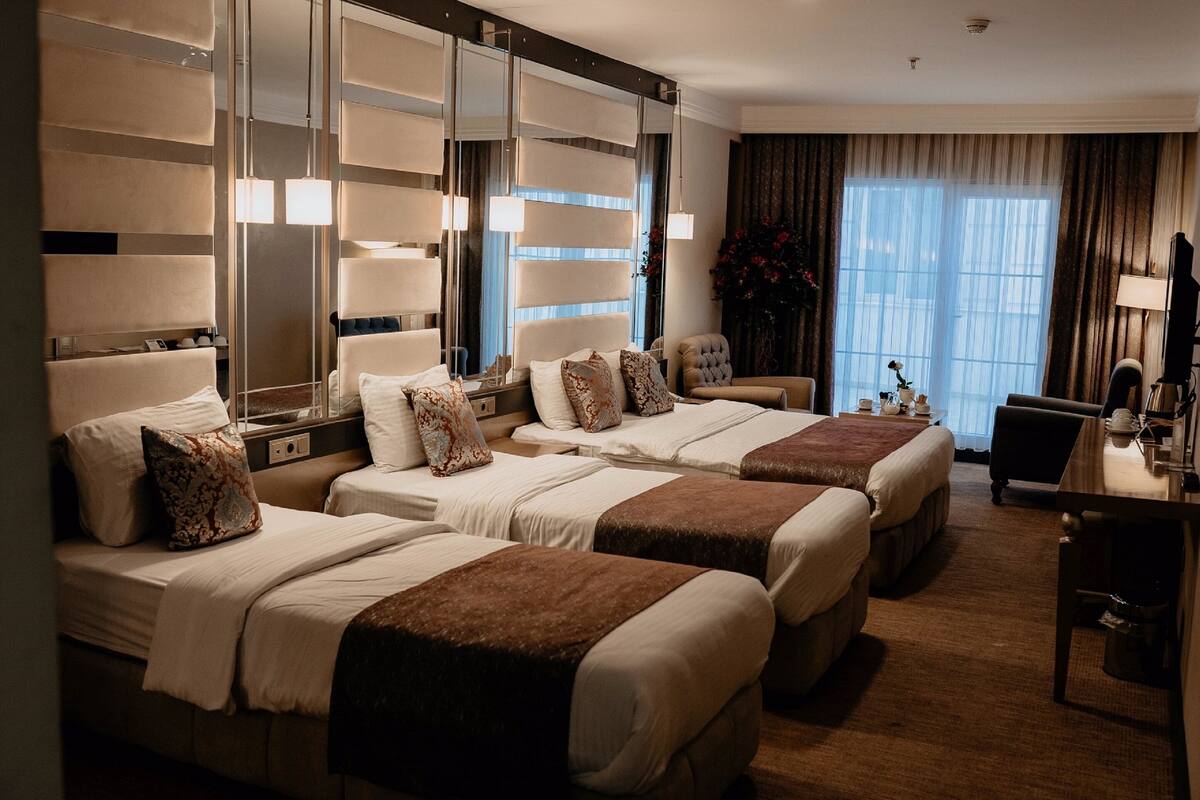 A hotel room with three beds, a desk, and a large mirror.