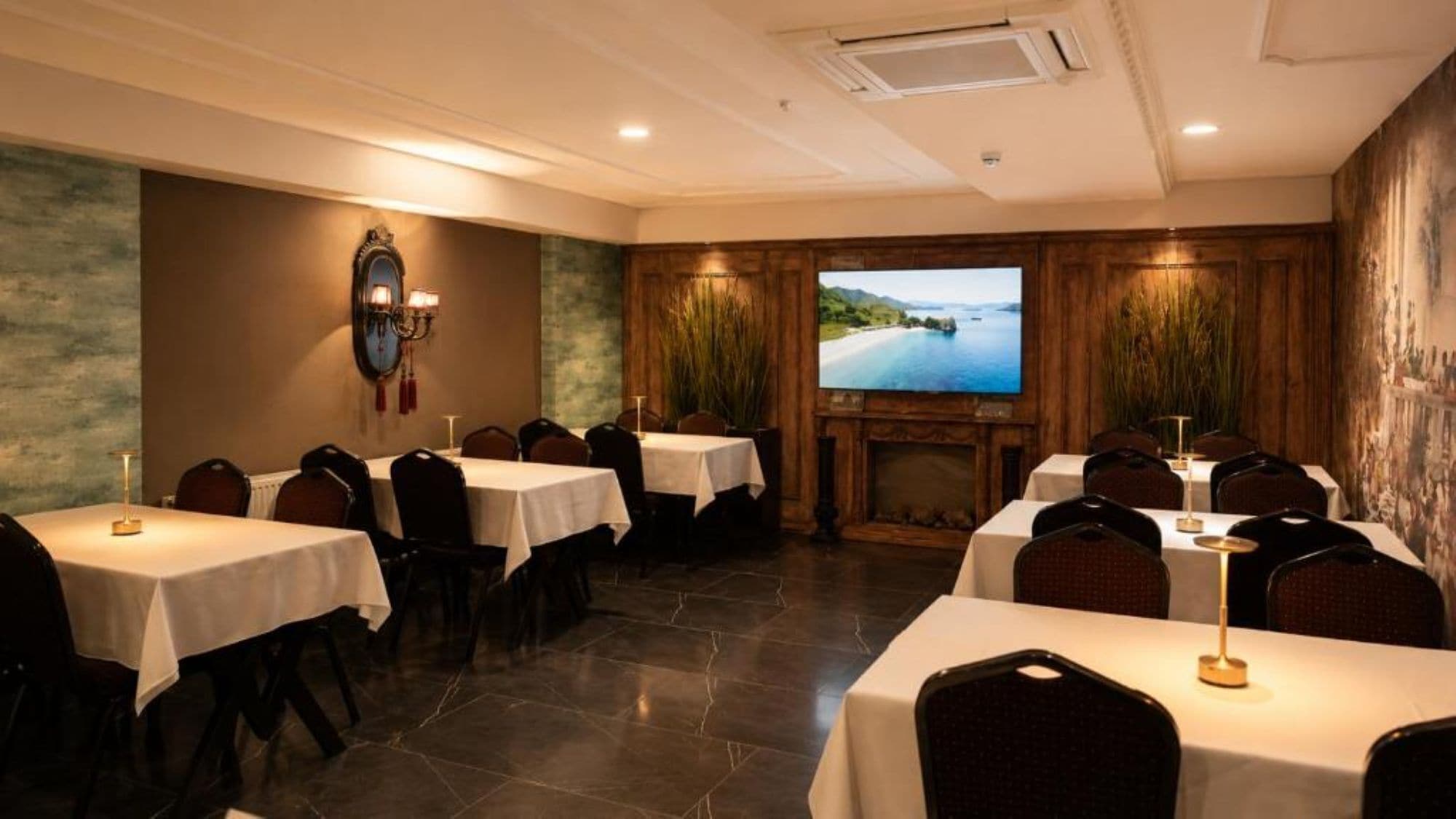 A conference room with multiple tables, chairs, a fireplace, and a large screen displaying a scenic view.
