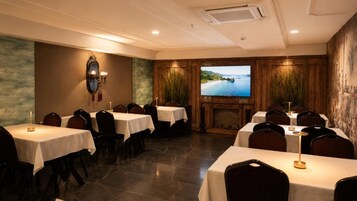 Un salón de conferencias con varias mesas, sillas, una chimenea y una pantalla grande que muestra una vista panorámica.