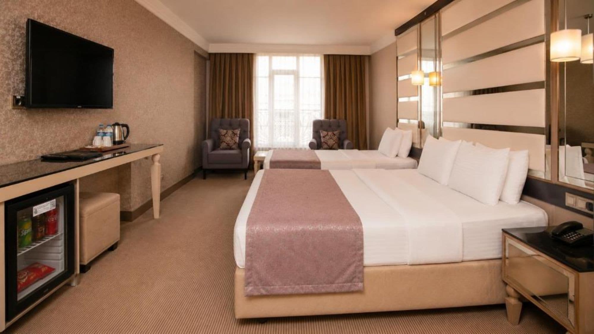 A hotel room with two beds, a television, a minibar, and a seating area with chairs.