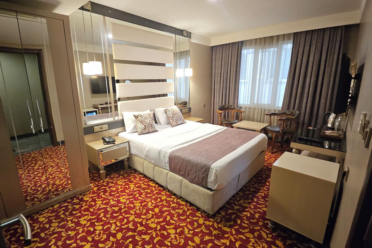 A hotel room with a large bed, a desk, a mirror, and a wardrobe.