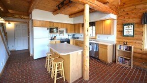 Una cucina con mobili in legno, un'isola centrale con sgabelli, un pavimento in mattoni e un soffitto in legno.