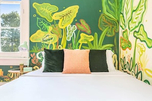 Un letto con due cuscini, una finestra e un murale con motivi vegetali sulla parete.