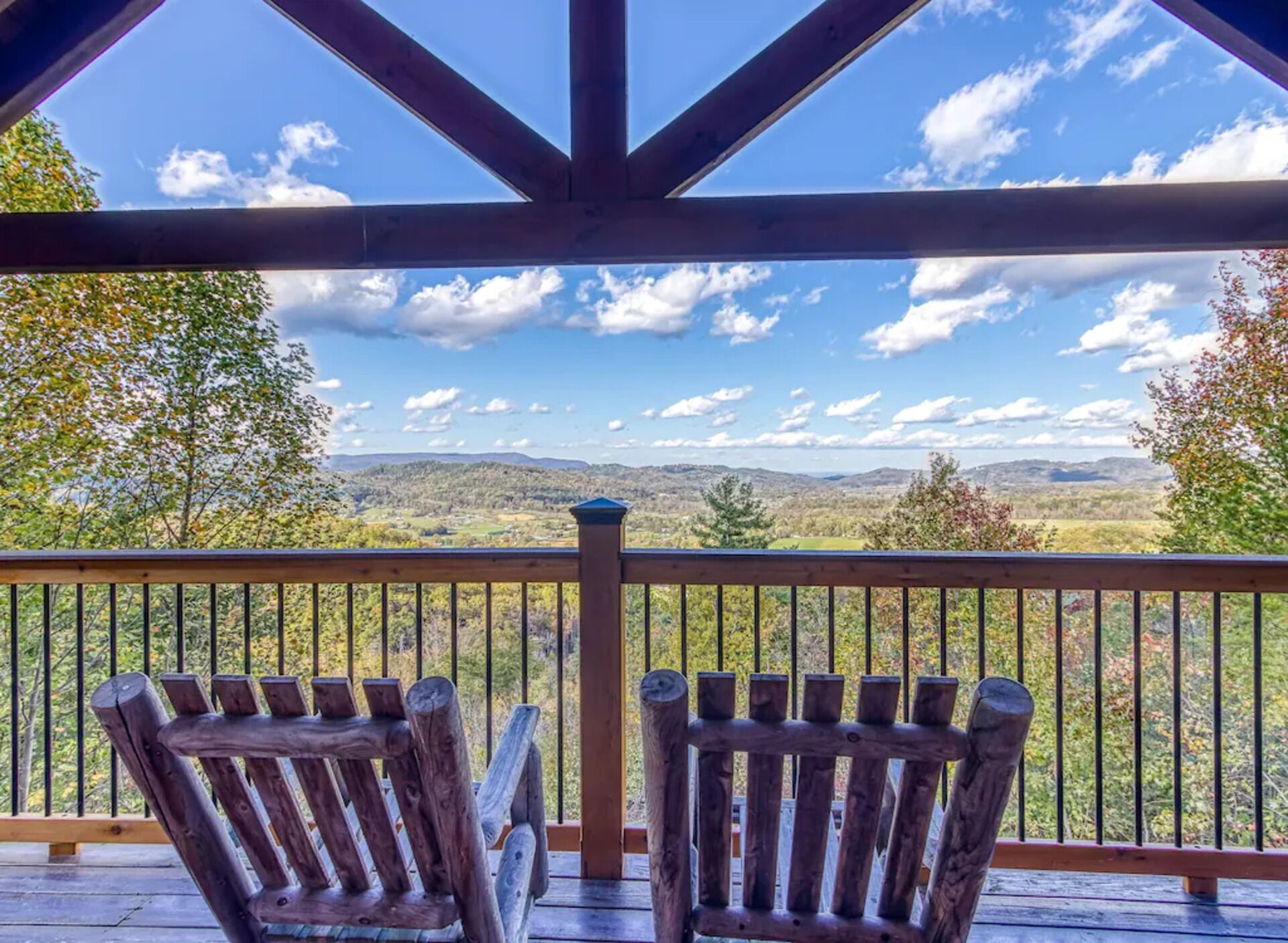 Eine Holzterrasse mit zwei Adirondack-Stühlen, die einen schönen Ausblick auf Hügel und Bäume unter blauem Himmel bietet.