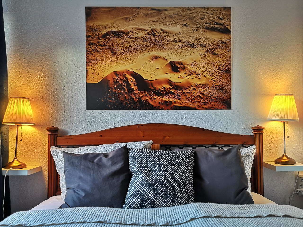 A bed with a wooden headboard, two bedside lamps, and a large landscape painting above the bed.