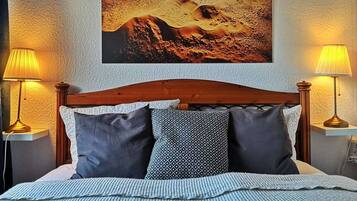 A bed with a wooden headboard, two bedside lamps, and a large landscape painting above the bed.