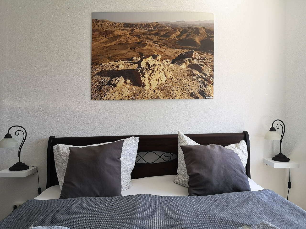 A bed with a headboard, two bedside tables with lamps, and a wall-mounted painting.