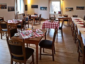 A dining area with multiple tables and chairs, each covered with a red and white checkered tablecloth. The room has wooden flooring and walls adorned with framed pictures. - Landlust Hotel (Gransee)