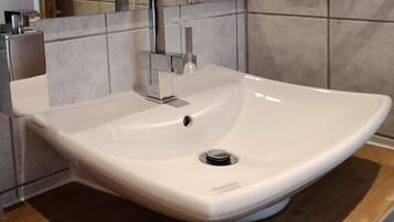A white ceramic sink with a single faucet, set in a modern bathroom with tiled walls and a wooden countertop.