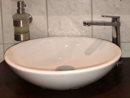 Un lavabo de cerámica blanca redondo con un solo grifo, un dispensador de jabón y un espejo.