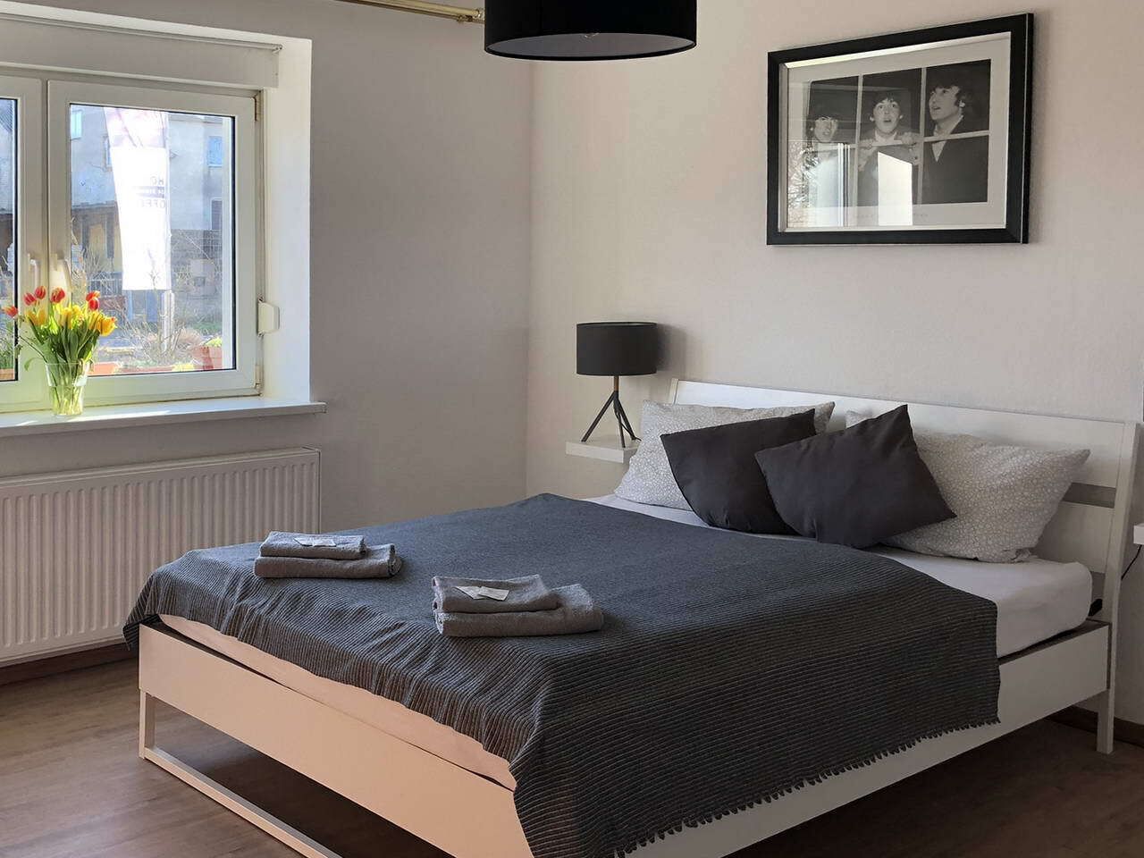 Un dormitorio con cama, mesita de noche, lámpara y una foto en el marco en la pared.