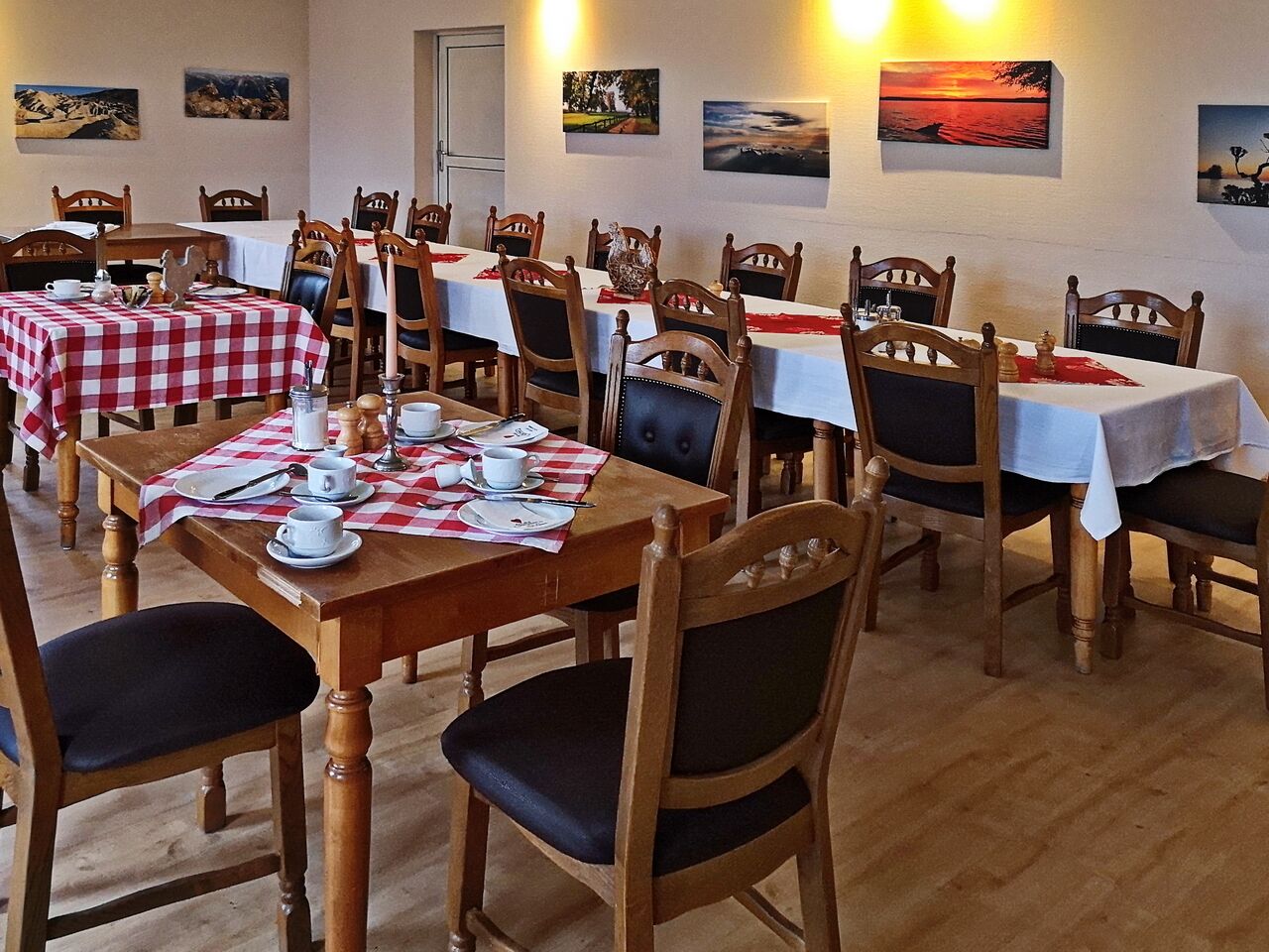 Un comedor con varias mesas dispuestas para comidas, sillas de madera y obras de arte en las paredes.