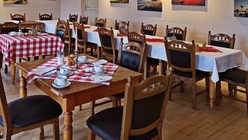 Un comedor con varias mesas dispuestas para comidas, sillas de madera y obras de arte en las paredes.