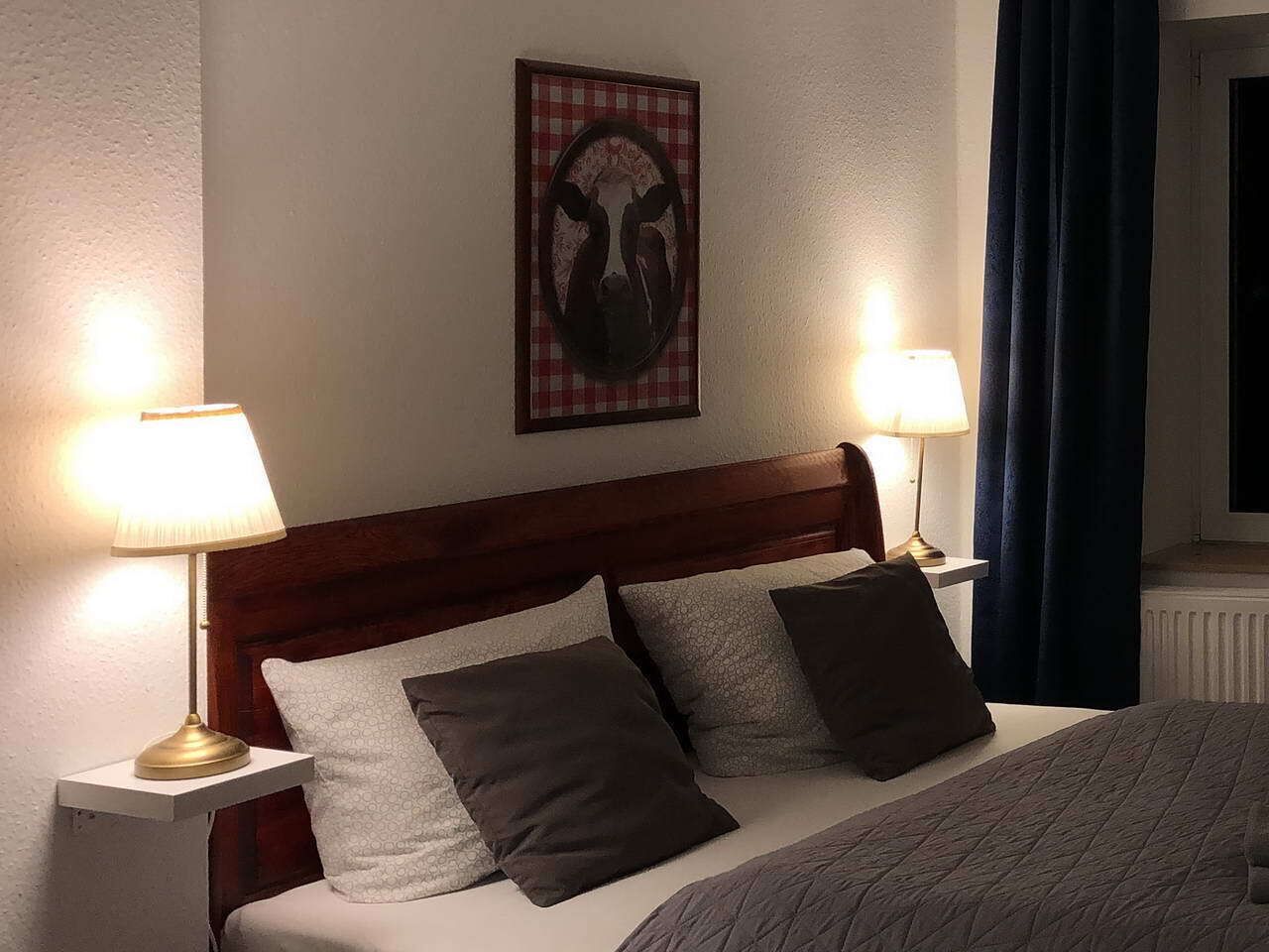 A hotel room with a bed, two bedside lamps, a headboard, and a wall-mounted artwork.