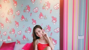Cama com papel de parede temático do Hello Kitty, mesa de cabeceira com um telefone e parede listrada.