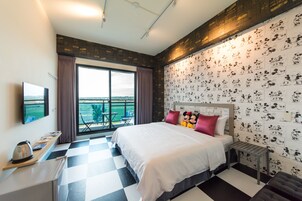Habitación de hotel con suelo de cuadros, una cama grande con ropa de cama blanca, cabecera con diseños de Mickey Mouse, un televisor de pantalla plana en la pared y vistas al exterior a través de un ventanal amplio.