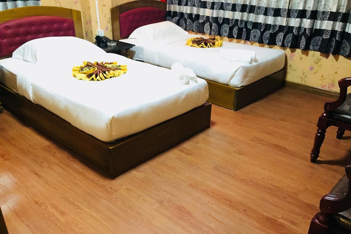 Two beds with white linens, a wooden floor, and a red upholstered headboard.