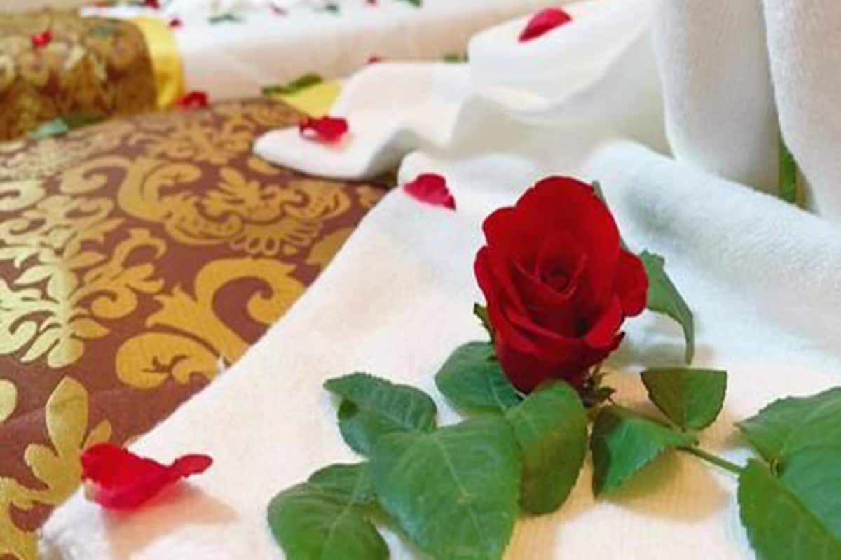 A bed with white linens and a red rose on the bedspread.