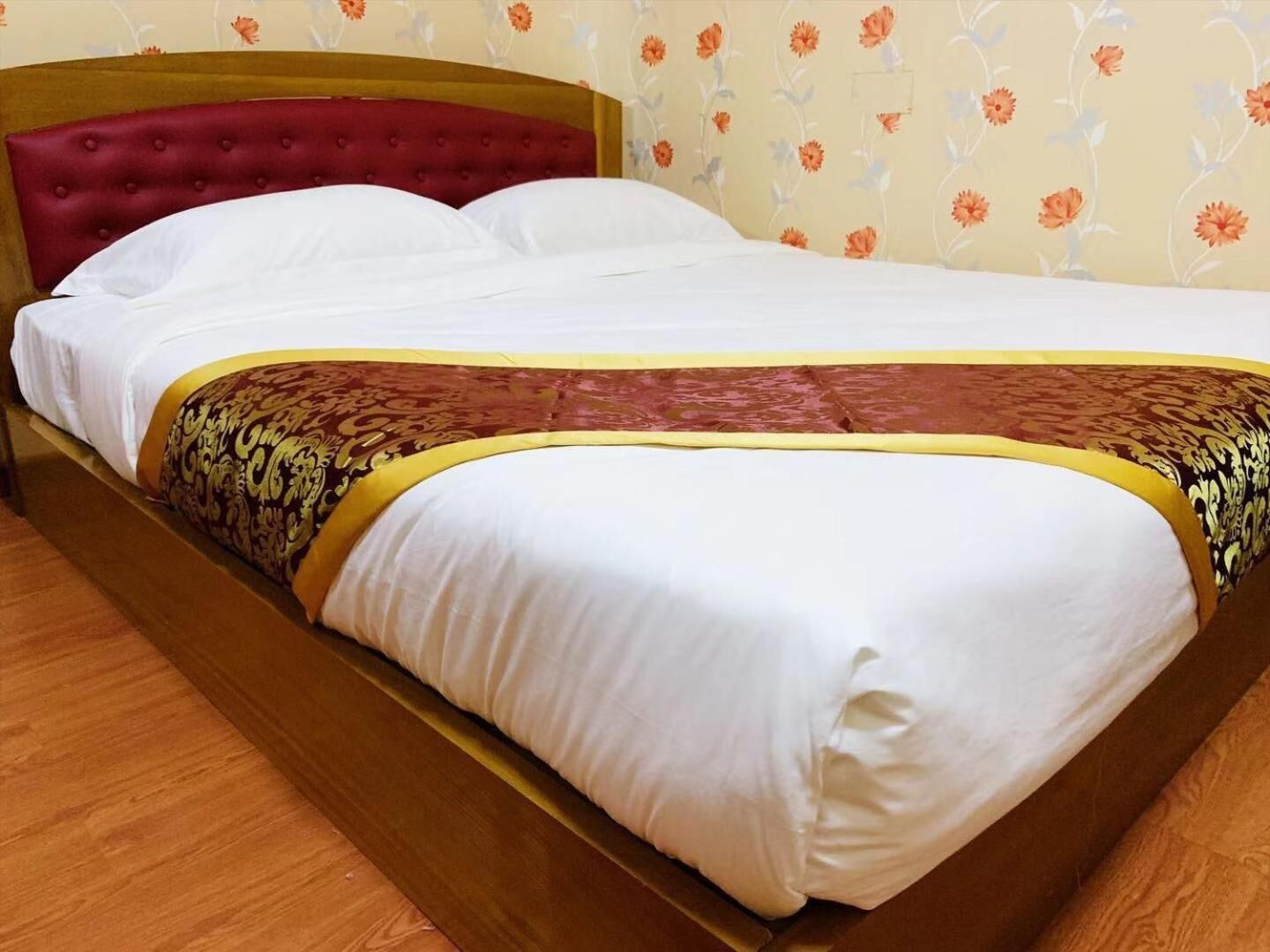 A bed with a red headboard, white bedding, and a floral wallpaper pattern.
