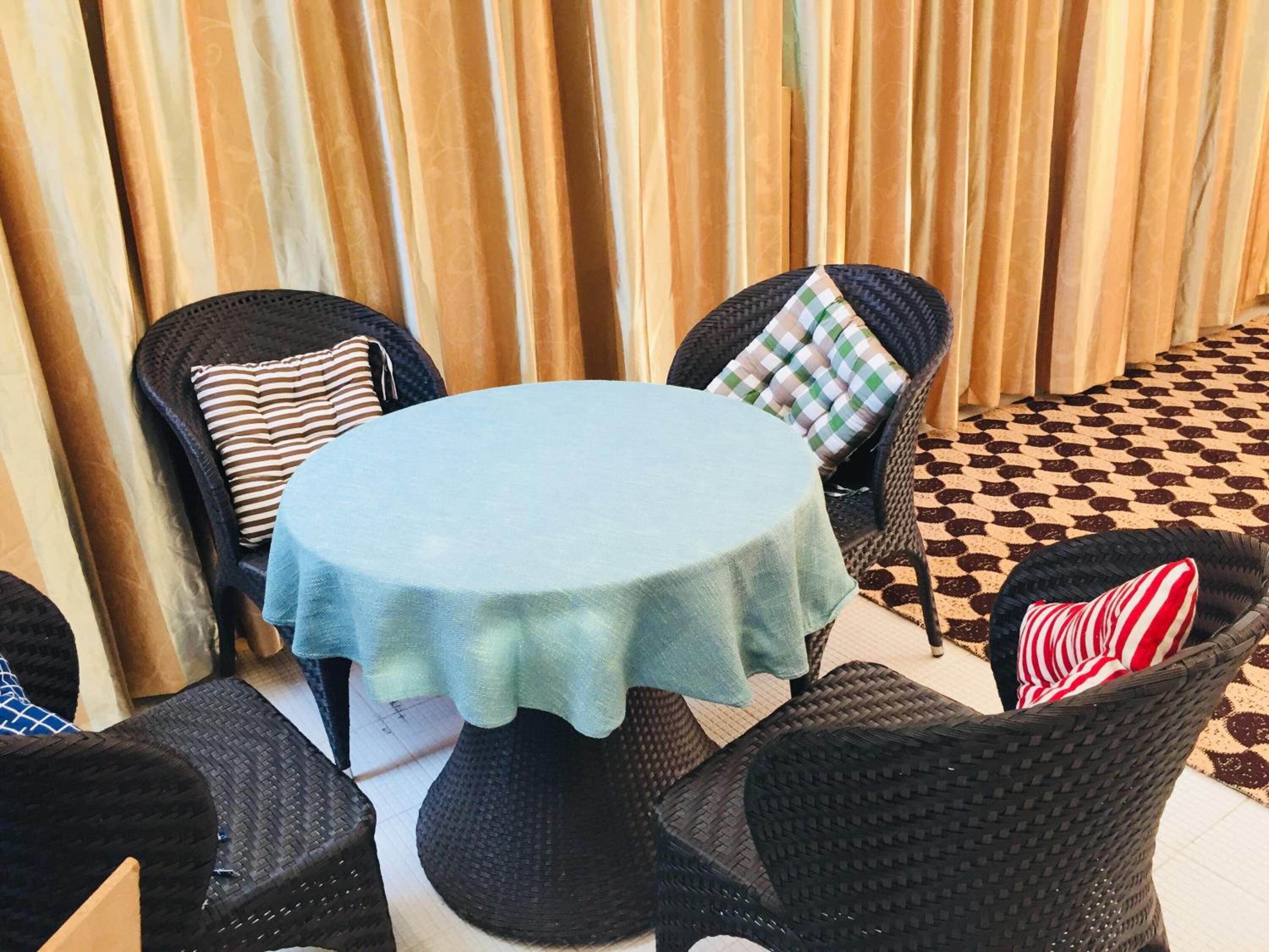 A round table with a light blue tablecloth, surrounded by black wicker chairs with striped and checkered cushions.