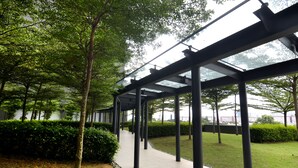 A covered walkway with a tiled floor, surrounded by greenery and trees.