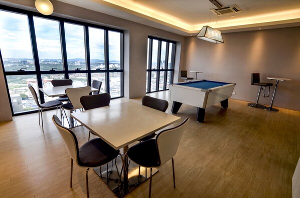 Una habitación moderna con mesa de billar, comedor y ventanas amplias con vista a la ciudad.