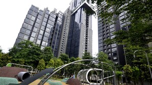 A playground with slides and swings, surrounded by trees and tall buildings.