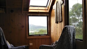 Una habitación con paredes de madera, un tragaluz, dos sillas estampadas y una cama con colcha.