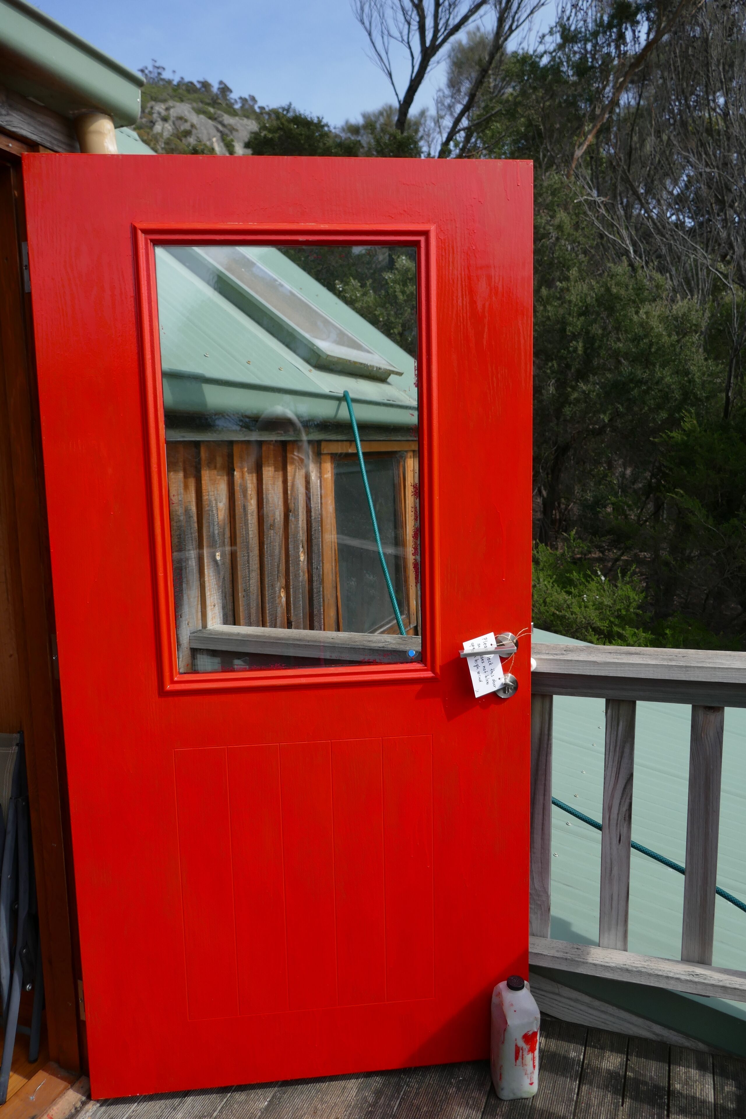A red door with a window, a wooden deck, and a white object on the ground.