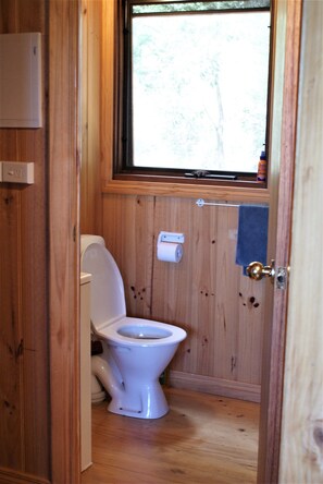 Een klein houten badkamertje met een toilet, een raam en een handdoek aan de muur.