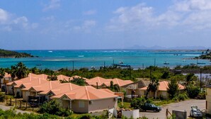 A coastal residential area with houses, a road, and a view of the sea with boats. - Villa Jwi Lavi Boutique Hotel (Cul de Sac)