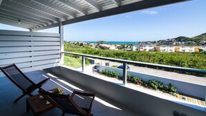 A balcony with two lounge chairs and a small table, overlooking a coastal area with buildings and greenery. - Villa Jwi Lavi Boutique Hotel (Cul de Sac)
