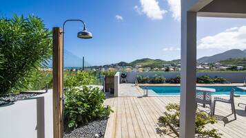 A wooden deck with a pool, a pergola, and a view of a hilly landscape.