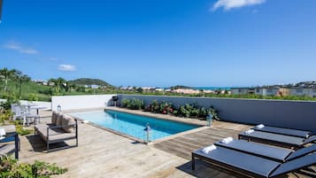 Una piscina al aire libre, sombrillas, sillones reclinables de piscina