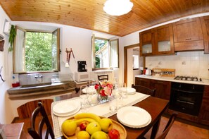 Uma cozinha com armários de madeira, uma mesa de jantar posta para dois e uma janela com vista para o verde lá fora.