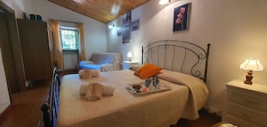 Una cama bien hecha con una bandeja de alimentos para el desayuno, una lámpara de noche y una ventana con cortinas.