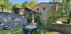A stone building with a tiled roof, a stone wall, and a small garden with a table and chairs. - Wonderful private villa for 7 people with WIFI, private pool, TV, terrace and pets allowed (Bagni Di Lucca)