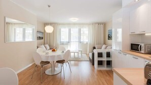 Quarto moderno e bem iluminado, com mesa de jantar, cadeiras, sofá e cozinha equipada com armários e micro-ondas.