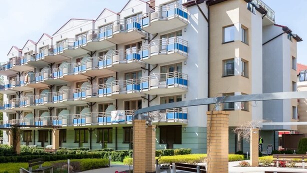 Um edifício residencial com vários andares, varandas, um pátio ajardinado e um caminho de tijolos.