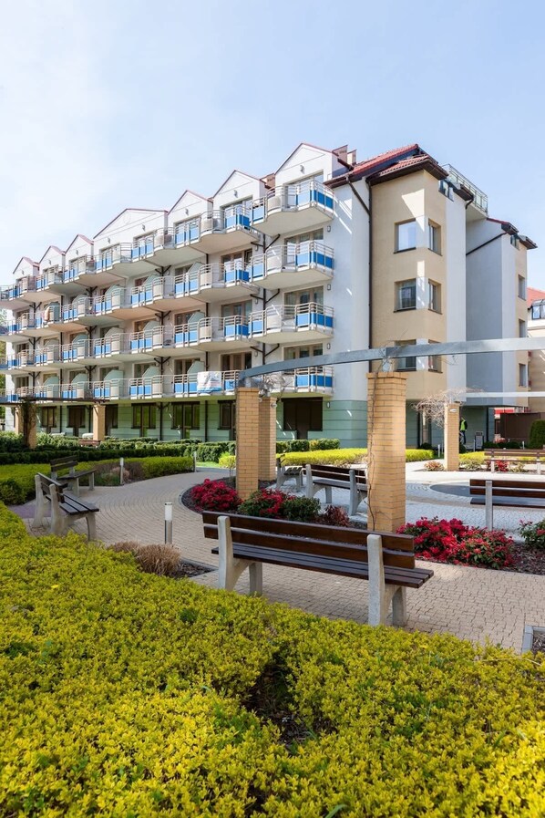 A multi-story residential building with balconies, a landscaped courtyard, and a brick pathway.