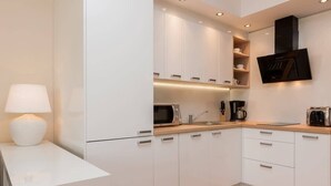 Cozinha moderna com armários brancos, micro-ondas embutido, máquina de café e televisão de tela plana montada acima do balcão.