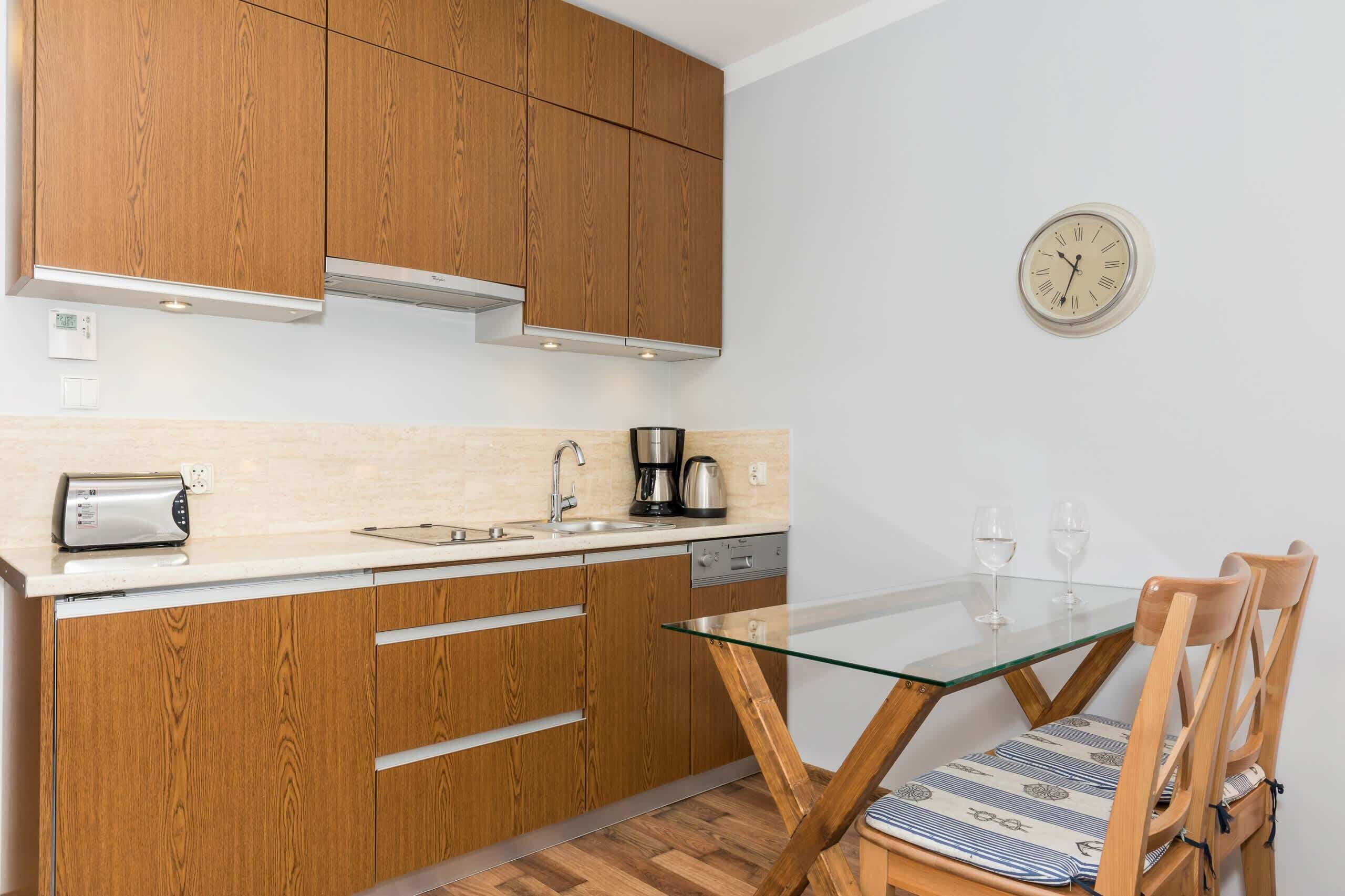 Een moderne keuken met houten kastjes, een eettafel met glazen blad en een wandklok.