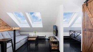 Un dormitorio tipo loft con tragaluces, un sofá, una mesa de centro y un televisor montado en la pared.